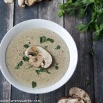 Keto Cream of Mushroom Soup in a white bowl on a dark barn wood background with fresh mushrooms and parsley.