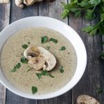 Keto Cream of Mushroom Soup in a white bowl on a dark barn wood background with fresh mushrooms and parsley.