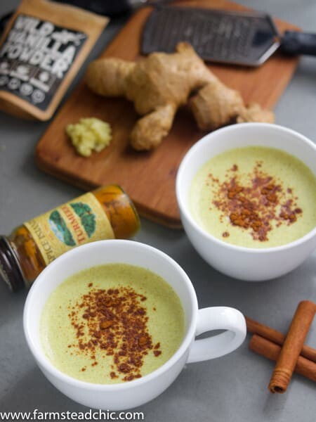 Two Paleo and Whole30 Ginger Turmeric Lattes with cinnamon sticks, fresh ginger and a bottle of ground turmeric. 