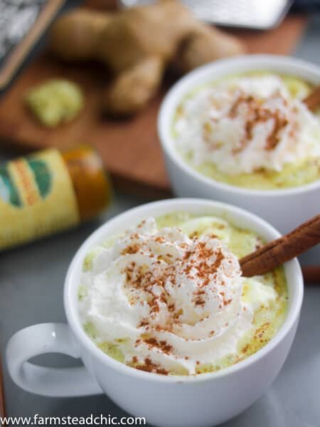 Two Paleo and Whole30 Ginger Turmeric Lattes with cinnamon sticks, fresh ginger and a bottle of ground turmeric. 