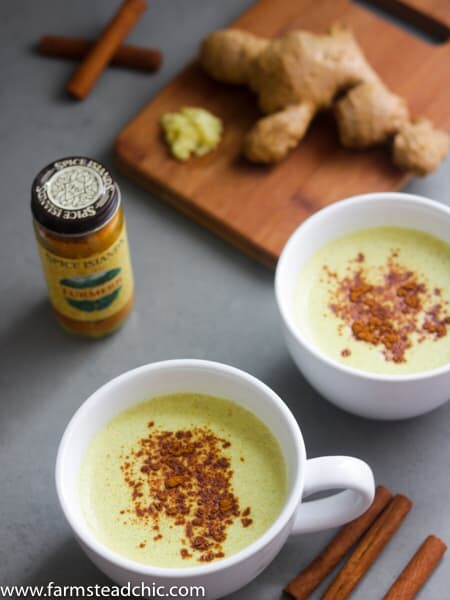 Two Paleo and Whole30 Ginger Turmeric Lattes with cinnamon sticks, fresh ginger and a bottle of ground turmeric. 