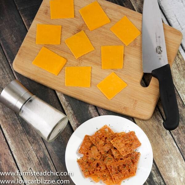keto crackers with a cutting board and knife, slices of fresh cheese and a salt grinder