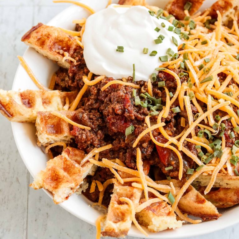 Chow down on these Low Carb, Keto Chili Cheese Chaffle Fries when you're craving some real comfort food. Perfectly firm and crispy chaffles are sliced into "fries," piled with meaty, beanless chili and topped with cheddar cheese, a hefty dollop of sour cream and a sprinkling of vibrant, flavorful chives.   
